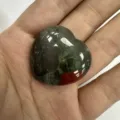 Nahaufnahme eines herzförmigen Blutstein-Ornaments, gehalten in der Hand, zeigt Textur. - 20x6mm / Drachenblutstein