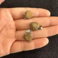 Drei 12 mm herzförmige Natursteinanhänger mit Silberösen, auf einer Handfläche präsentiert - 12x6mm / Landschaftsjaspis