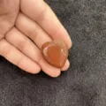 Vue détaillée d'un cabochon en pierre d'or brun étincelant en forme de cœur tenu à la main - Pierre de Sable Dorée / 10mm