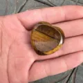 Detailansicht eines polierten herzförmigen Tigerauge-Sorgensteins in der Handfläche - Tigerauge / 30mm