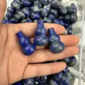 Makro-Detail einer Hand, die polierte blaue Lapislazuli-Stein-Anhänger in Kalebassenform hält - Ca. 18*30mm / Natürlicher Lapislazuli