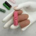 Gedetailleerde close-up van een roze natuurstenen bamboeknoop met twee gaten in de hand. - Rozerood