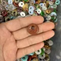 Close-up of a goldstone donut bead held in hand with assorted crystal stones background. - 14mm / Gold Sandstone