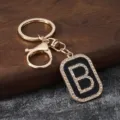 Close-up of a stylish gold-tone letter B keychain with rhinestones and black enamel accent. - Letter B