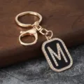 Close-up detail of the sparkling rhinestone letter M pendant on the gold keychain. - M