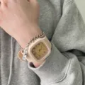 Nahaufnahme am Handgelenk: Beige Silikonuhr mit Metallkettenarmband und Anhänger. - Gebrochenes Weiß