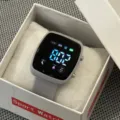 Gedetailleerd weergave van vierkant digitaal sporthorloge met grijze band in witte geschenkdoos. - donkergrijs