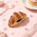 Detaillierte Nahaufnahme des süßen Simulations-Croissant-Kühlschrankmagneten im rosa Dessert-Set. - Schokoladen-Croissant