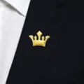 Close-up view of a luxurious gold crown brooch pinned on a dark suit lapel, premium detail. - Crown / Gold