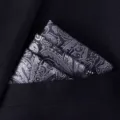 Detailopname van een zilveren paisley pochette, netjes gevouwen in de borstzak van een donker pak. - X8905 (Zwart Zilver Paisley)