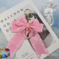 Close up of a cute pink pleated ribbon bow keychain with pearl heart charm and metal clasp. - Pink