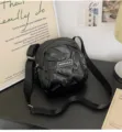 Detailansicht der schwarzen gesteppten Umhängetasche mit verstellbarem Riemen und Label. - Schwarz