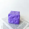 Nahaufnahme eines lila käseförmigen Squishy-Spielzeugs zum Stressabbau auf Papierhintergrund - Käse / 5x5x5 / Lila