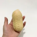 Nahaufnahme eines erdnussförmigen Squishy-Stressspielzeugs, das in der Hand gedrückt wird - Beige