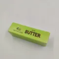 Nahaufnahme eines grünen Butterstick-Squishy-Stressabbauspielzeugs mit Etikett - Kleiner Grüner Stil