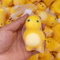 Niedliches gelbes Slow-Rebound-Quetschspielzeug in einem schützenden Netzbeutel in der Hand - Kleiner Milchdrache / 8cm
