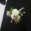 Boutonniere detail shot showing elegant white and blue artificial flowers on a black suit lapel. - Corsage / Light Bean Paste