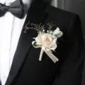 Elegant white rose wedding boutonnière with green leaves and ribbon for groom, suit jacket. - Beige Boutonniere