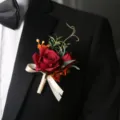 Red rose boutonniere with beige ribbon and green leaves, perfect for wedding groom and suit decor. - Red Boutonniere