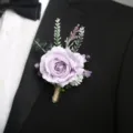 Vista dettagliata dell'elegante bottoniera di rosa viola artificiale spillata su una giacca da abito. - Corsage / Viola chiaro