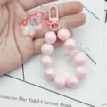 Gros plan détaillé de la lanière de téléphone en perles roses avec pendentif ourson. - Lapin en Perles / Rose