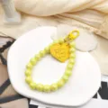 Gros plan détail du charme de téléphone en perles colorées et bracelet avec pendentif cœur. - Jaune