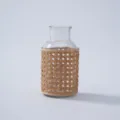 Detailed close up of transparent glass vase with woven rattan sleeve for rustic desktop decoration. - Style 1