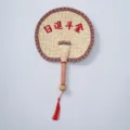 Detailed view of the handmade woven straw fan showing the classic red border and tassel decor. - Style 19