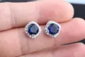 Nahaufnahme von eleganten quadratischen Halo blauen Zirkonia Ohrringen auf den Fingern. - Blau