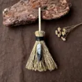Primo piano dettagliato di una mini scopa da strega con ciondolo di cristallo e manico in legno. - Scopa + Quarzo Rutilato