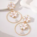Gros plan sur des boucles d'oreilles créoles creuses en métal avec fleurs et perles. - Blanc (JMX-ER9780)