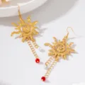 Gros plan de boucles d'oreilles pendantes soleil rétro dorées avec pampilles, perles et perles rouges. - Style Soleil à Gland de Perle (JMX-ER9629)