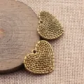 Nahaufnahme von antiker goldener geflochtener Herz-Anhänger auf Holzscheibe und Jute, Detail. - 1 Stück / Altgold