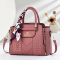 Close-up detail view of the pink embossed leather handbag featuring elegant handle silk scarf. - Pink