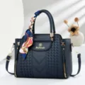Detailed view of the dark blue embossed leather handbag with chic handle scarf and side zippers. - Blue