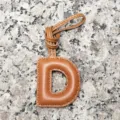Close-up detail of the light brown lambskin letter D bag charm showing stitching texture. - Letter D / Tan