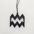 Black leather zodiac symbol pendant detail showing fine textured grain and hanging cord. - Black