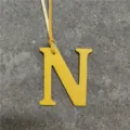 Close-up of yellow leather letter N bag charm pendant showing fine textured leather surface and strap. - Yellow