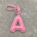 Close-up detail of a cute pink puffy leather letter A bag charm with white stitching strap. - Pink