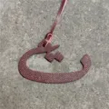 Close-up view of a maroon textured leather Arabic letter bag charm pendant detail. - Burgundy