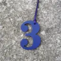 Close-up detail view of a blue textured leather number 3 bag charm with hanging strap. - Sapphire Blue