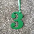 Close-up detail shot of a green leather number 3 charm with a light blue hanging cord. - Green