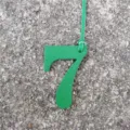 Primo piano del ciondolo per borsa numero 7 in pelle verde con trama fine e cinturino resistente. - Verde