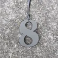 Detailed shot of a gray leather number 8 bag charm with fine strap on textured stone ground. - Gray