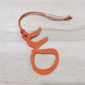 Detailansicht eines orangefarbenen Leder-Arabisch-Buchstaben-Taschenanhängers mit Kordel. - Orange