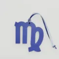 Detailed closeup view of a blue textured leather Virgo zodiac sign bag charm pendant. - Blue