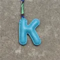 Detailaufnahme eines blauen Leder Buchstaben K Taschenanhängers mit buntem Schal. - K Himmelblau
