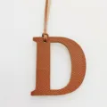Detail view of a stylish leather letter D bag charm with hanging strap, elegant accessory. - Brown