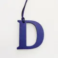 Detailed close-up view of a purple textured leather letter D bag charm with fine hanging strap. - Sapphire Blue
