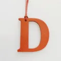 Orange leather letter D bag charm detail shot, elegant alphabet pendant accessory for purses. - Orange
